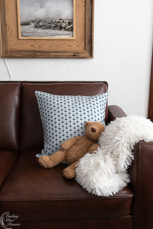 Leather couch with faux fur white throw, linen pillow, teddy bear, and white walls