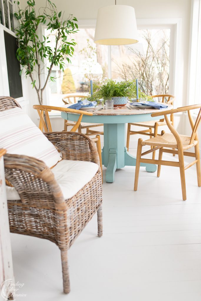 Sunroom with white walls, blue table, neutral chairs, white floor, white pendant light