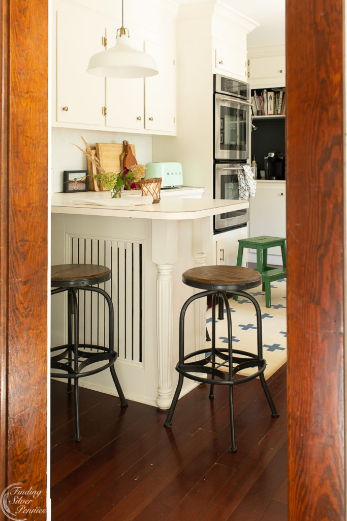 Kitchen with dark wood floor, white cabinets, white counters, and dark stools.