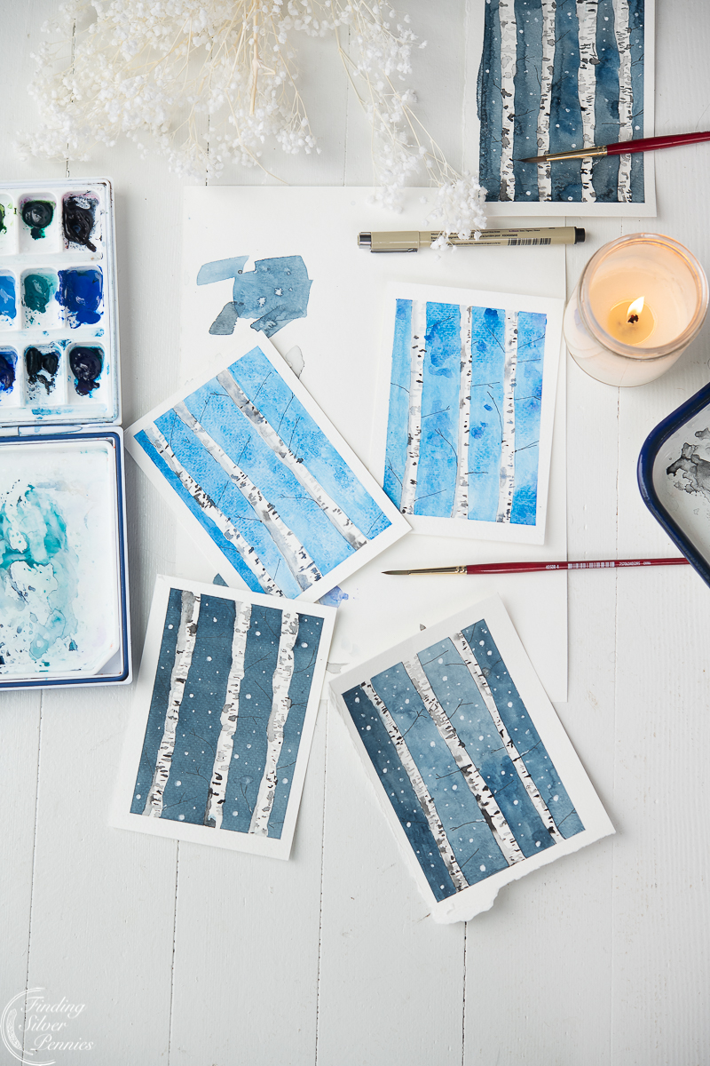 Birch Tree paintings with candle, paint brushes, and paints on white background